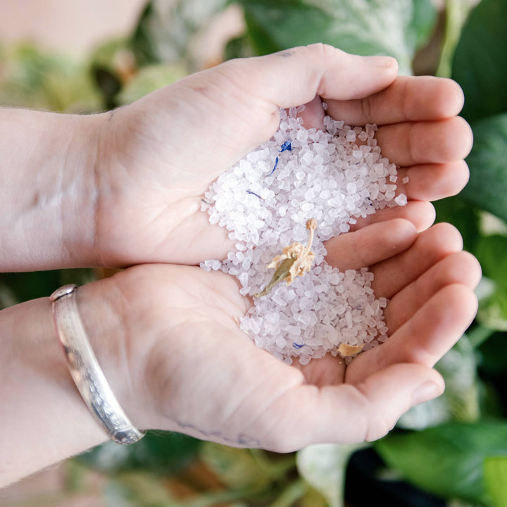 two hands cupping bath salt with some dried flowers. Brand: Lovewild Design