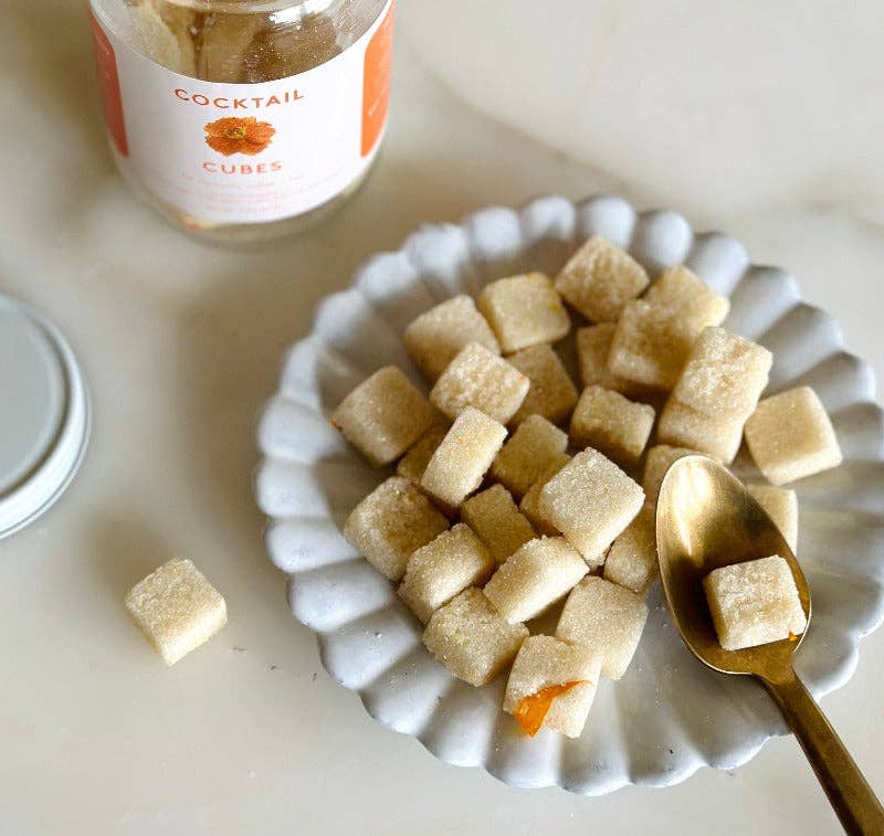 a white plate with sugar cubes and  a gold spoon with a jar of the sugar cubes in the background.