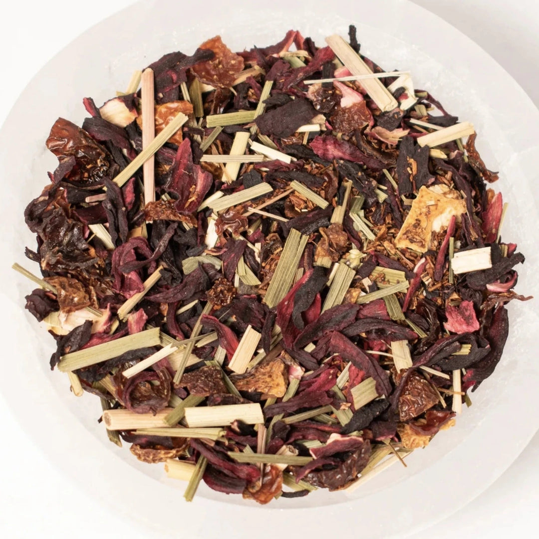 close up view of citrus hibiscus tea that contains dried up flowers and fruit in a white bowl.