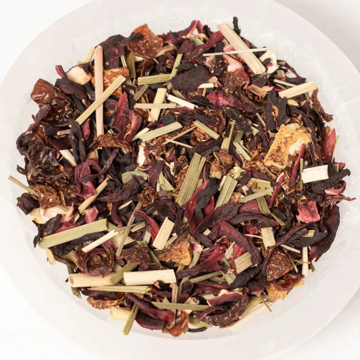 close up view of citrus hibiscus tea that contains dried up flowers and fruit in a white bowl.
