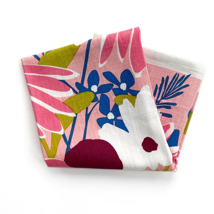 Folded Echinacea tea towel with a colorful floral design in pink, burgundy, blue, and white on a pink background.