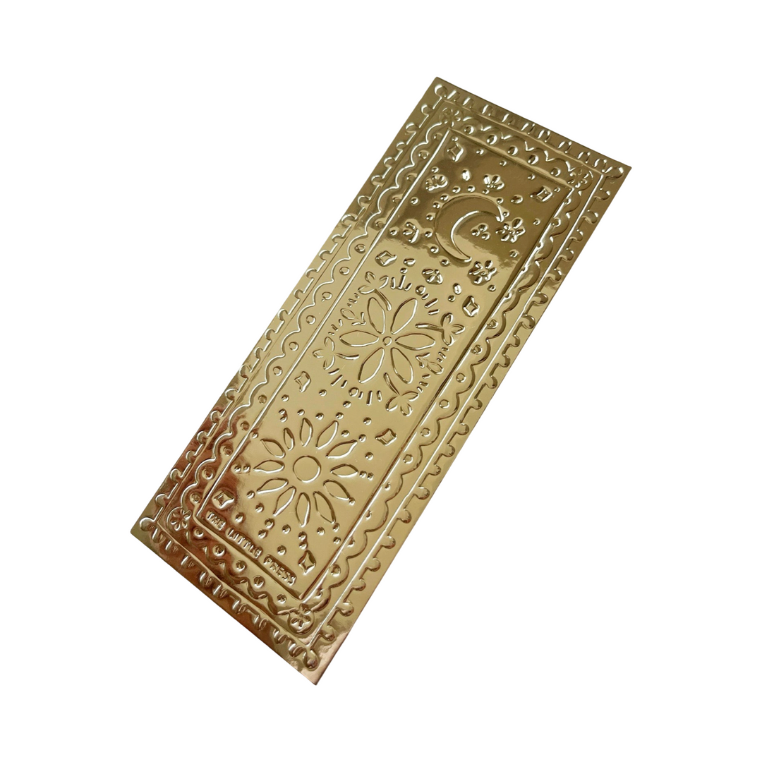 Gold faux-tin bookmark with embossed floral and celestial designs, including a sun, flower, and crescent moon