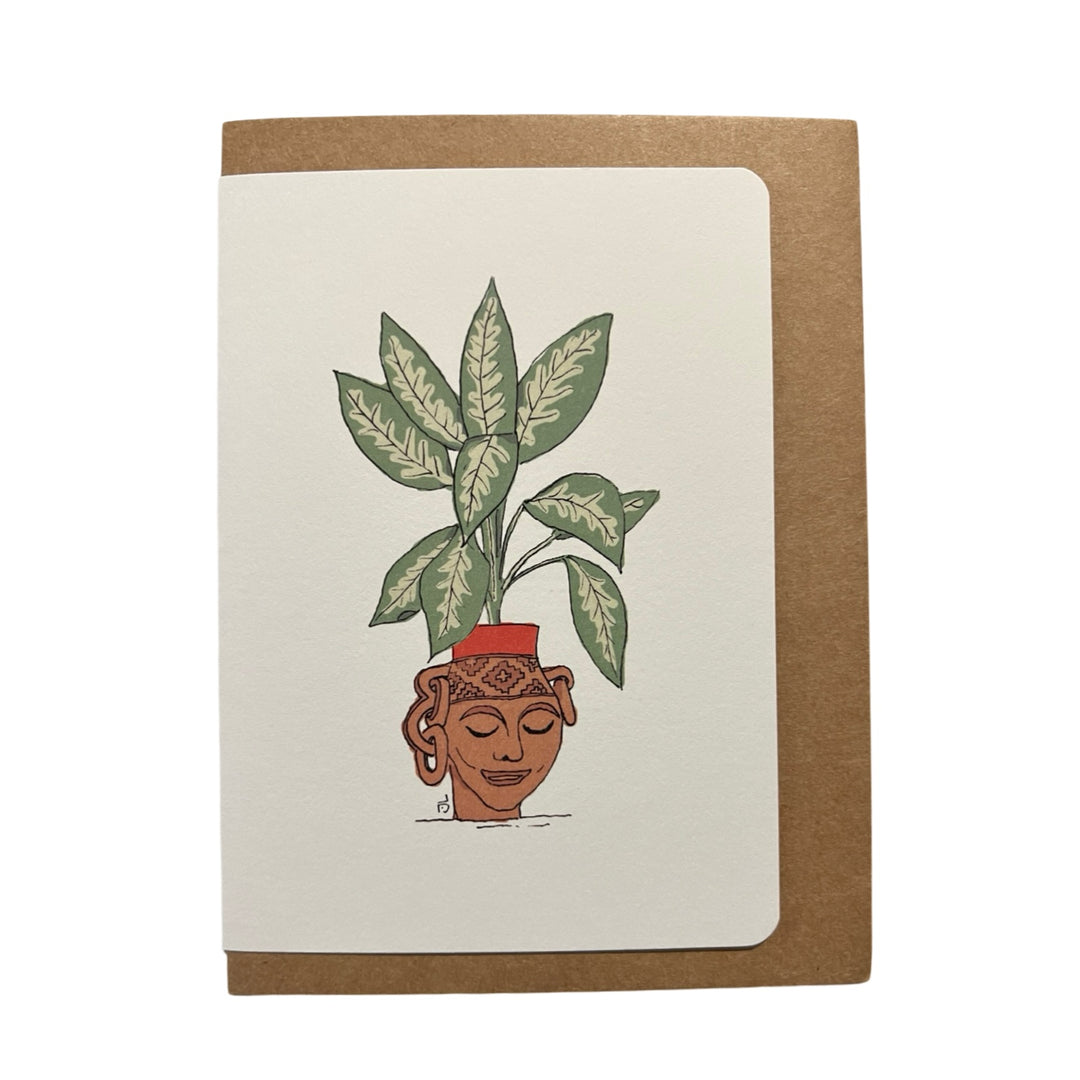 Illustration of a terracotta planter shaped like a serene face, filled with lush green leaves, featured on a greeting card with a kraft envelope in the background