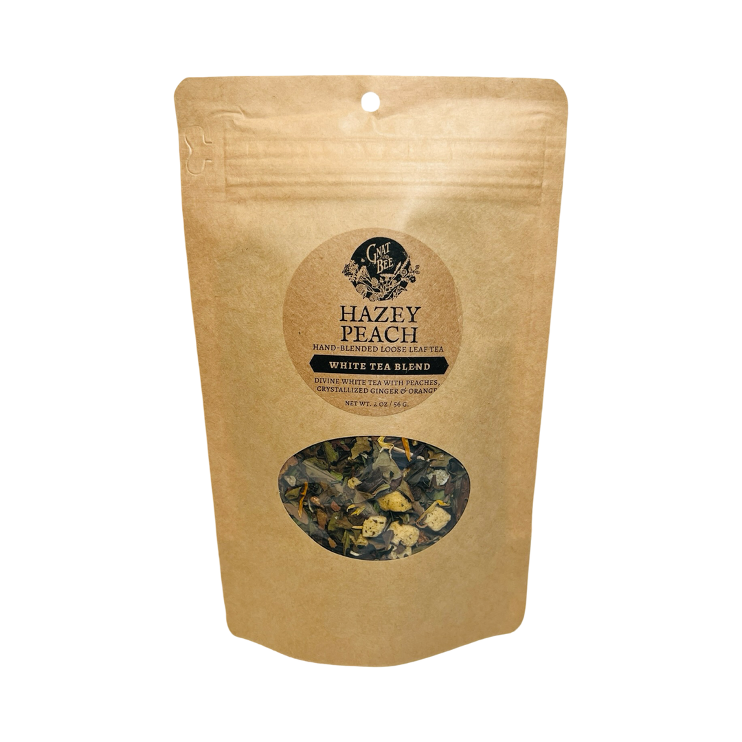 2 oz kraft pouch of Hazey Peach tea with a branded label and a clear window that displays the dried herbs and flowers that makes the tea.