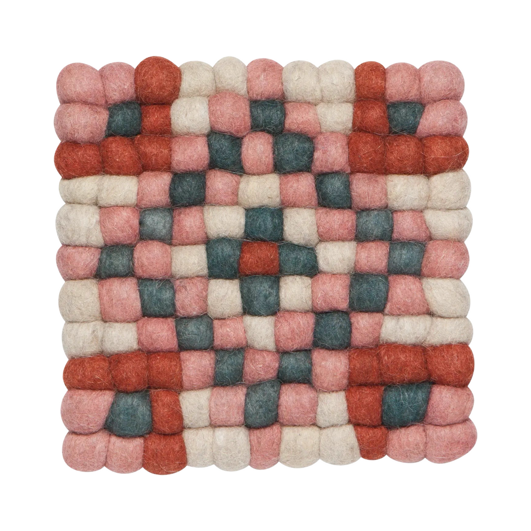 Handcrafted felted wool trivet with a checkerboard pattern in terracotta, blush pink, deep teal, and cream, designed to protect surfaces from heat.