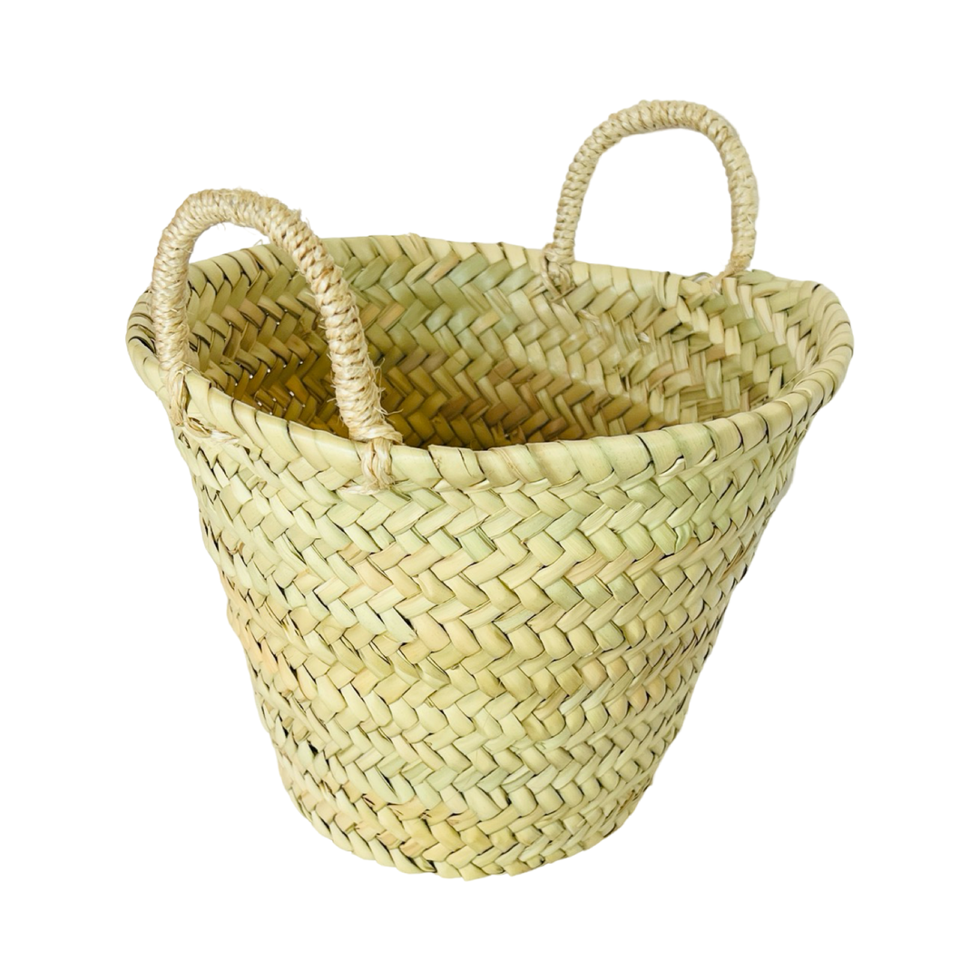 side view of a handwoven straw market basket made from natural palm leaves, featuring a wide, open-top design and sturdy braided handles.