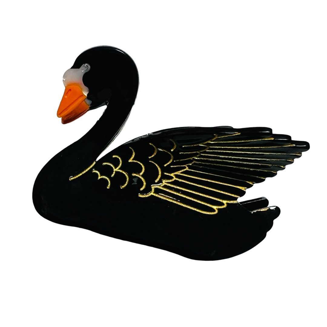 A swan-shaped hair clip with a black
finish, detailed wings, and an orange beak, set against a white background.