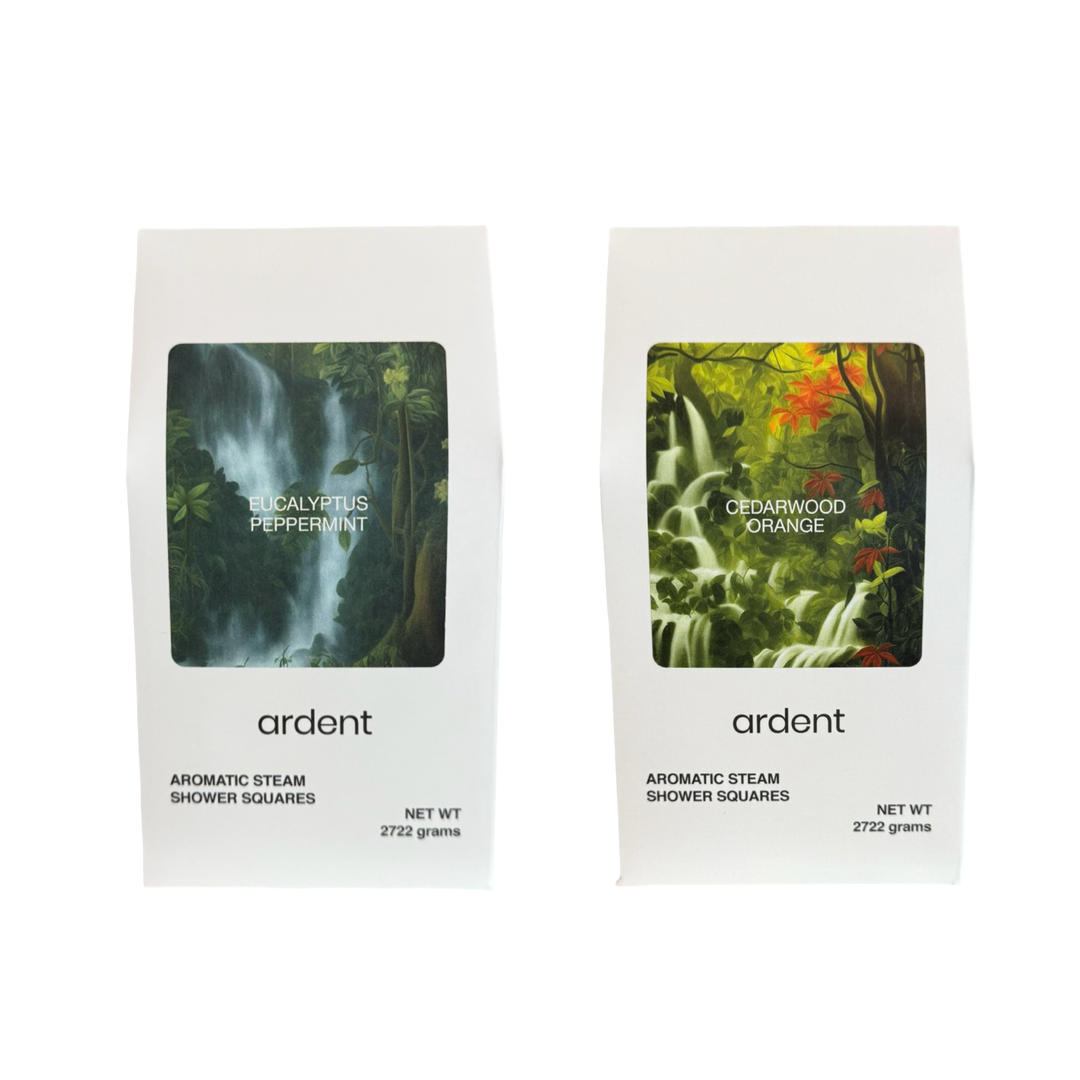 Two white packages of Ardent Aromatic Steam Shower Squares. The left package is labeled “Eucalyptus Peppermint” with a lush waterfall forest image. The right package is labeled “Cedarwood Orange” with a vibrant green forest and orange foliage image. Both packages state a net weight of 272.2 grams.