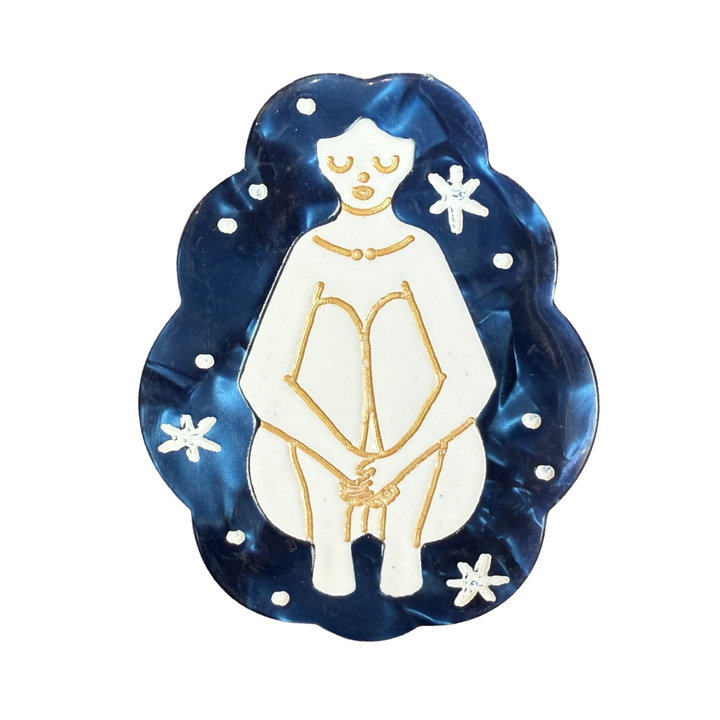 blue hair clip that features an outline of a woman in gold sitting down holding her knees in