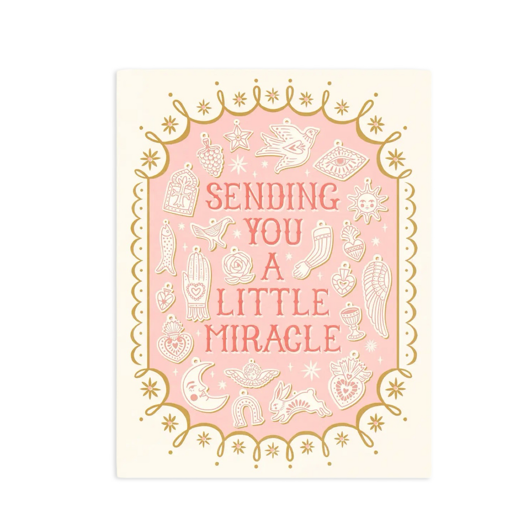 Cream colored card with a light pink center within a gold border with illustrations of various milagro charms featuring the phrase Sending You A Little Miracle in light pink lettering.