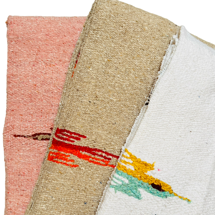 close up of three quarter folded woven blankets in the colors dusty pink, tan and white.