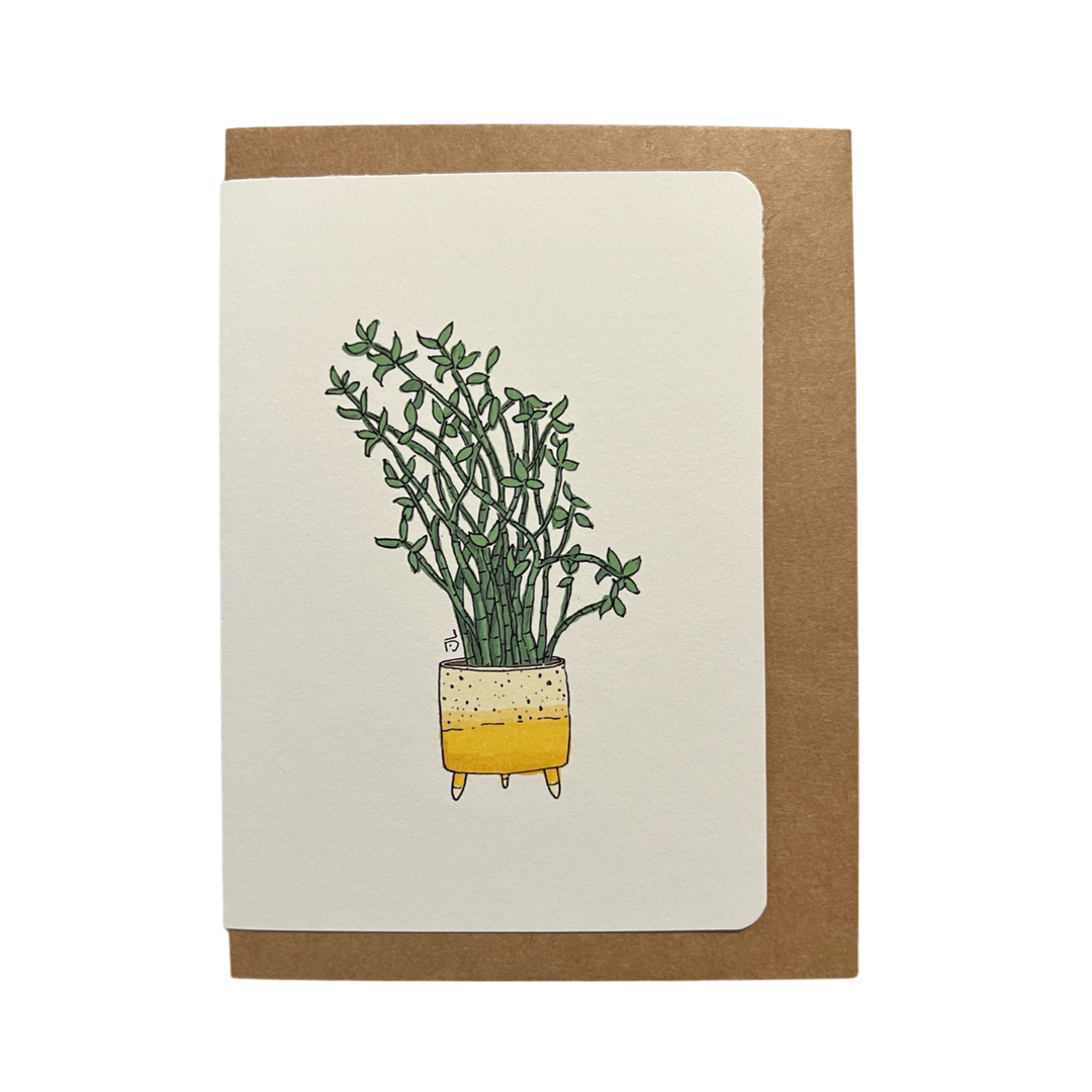 Illustration of a yellow and white ceramic planter filled with vibrant green leafy plants, displayed on a greeting card with a kraft envelope in the background.