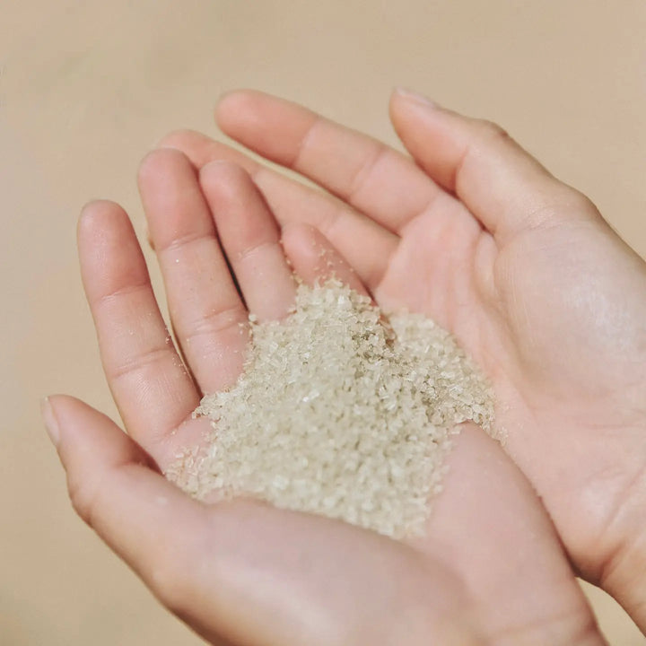 Close-up of hands holding translucent mineral bath soak crystals.