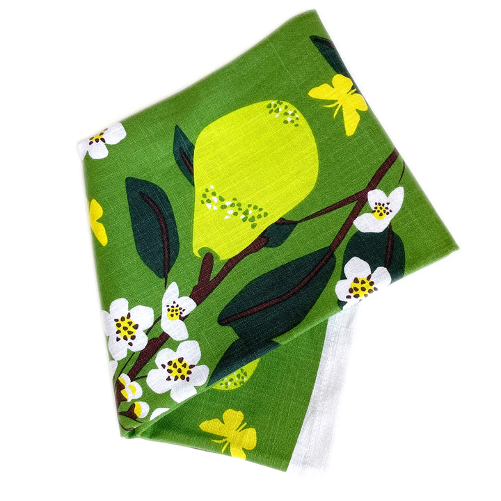 Folded green tea towel with a yellow pear, white blossoms, and butterfly print.
