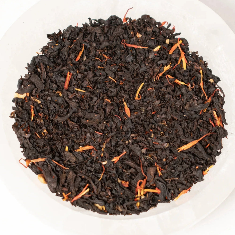 close up view of black tea with dried flower petals in a white bowl