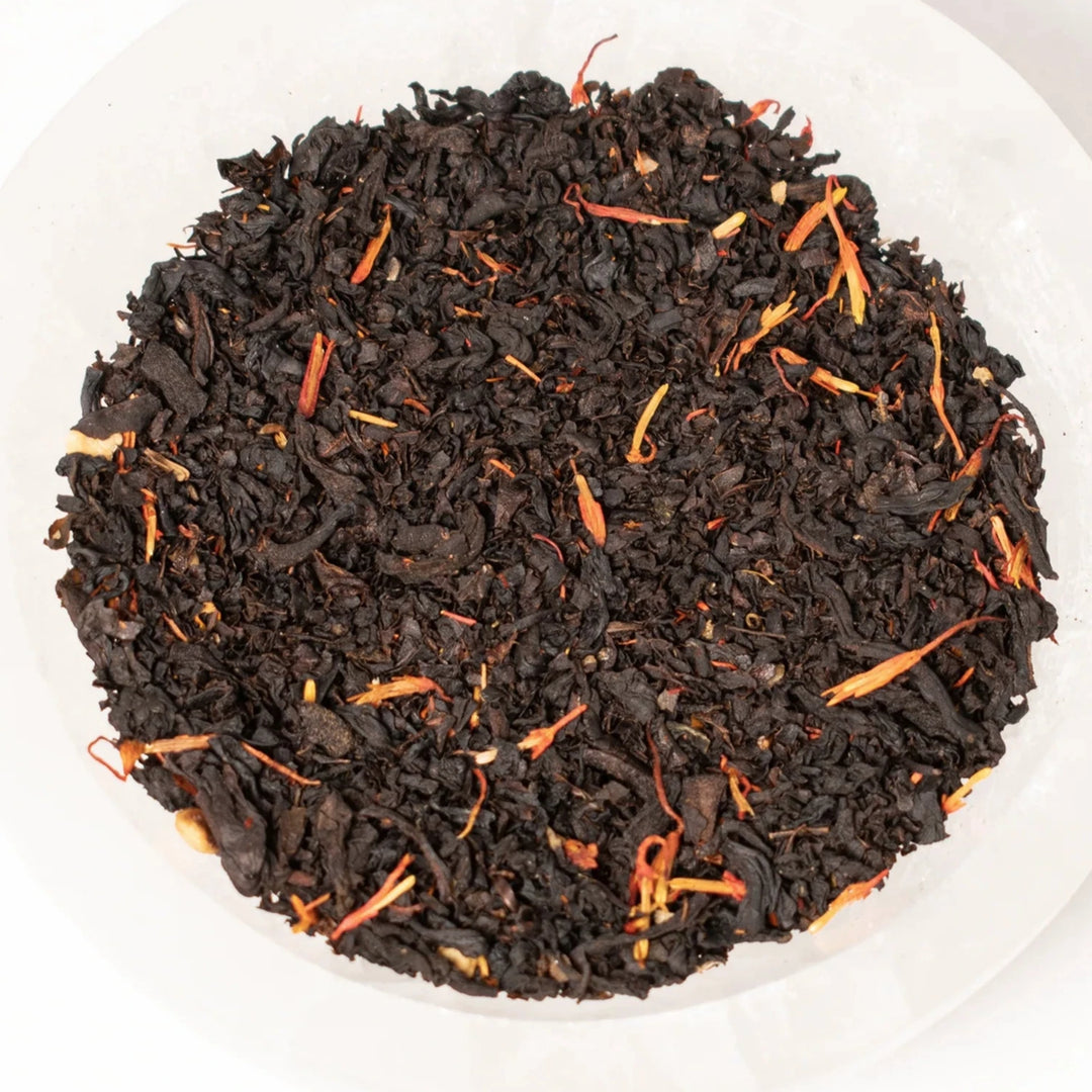 close up view of black tea with dried flower petals in a white bowl