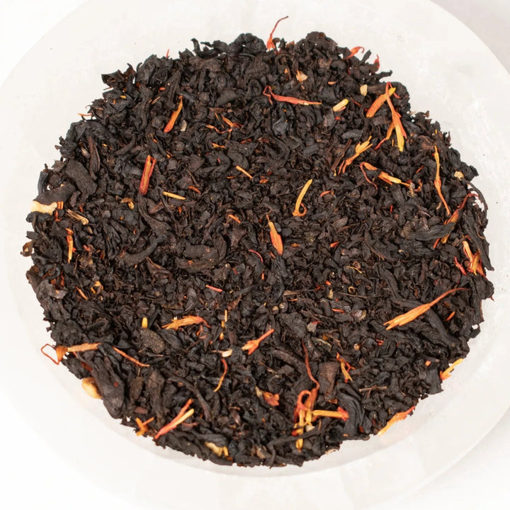 close up view of black tea with dried flower petals in a white bowl