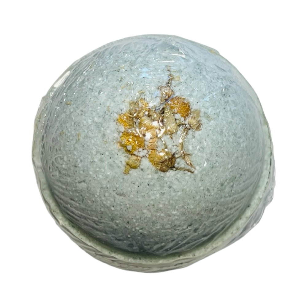 A single pale blue bath bomb with dried chamomile flowers on top, wrapped in clear plastic.