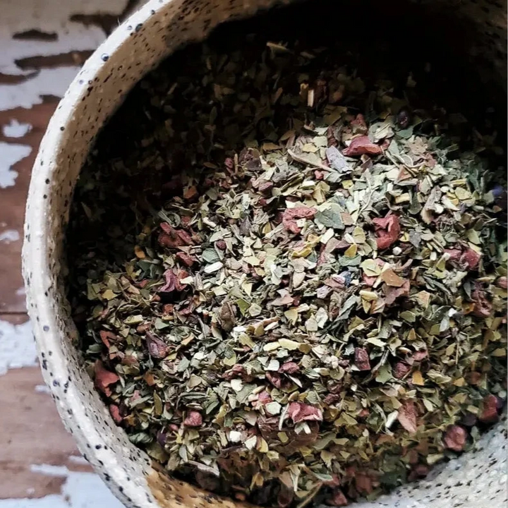 Ceramic bowl filled with loose leaf Cocoa Mint Mate tea blend, showing a mix of green yerba mate leaves, cocoa nibs, and mint.