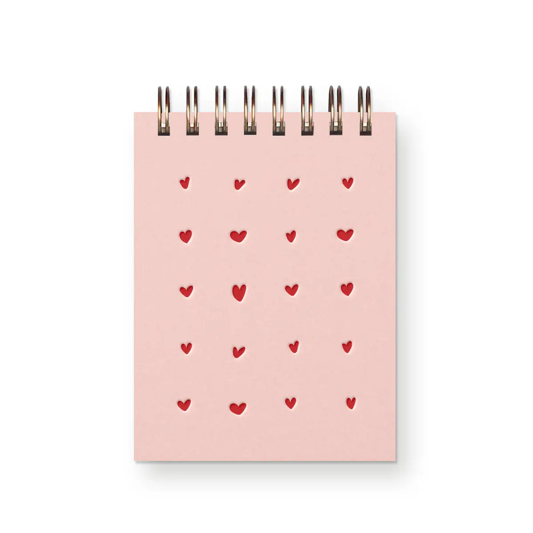 Small spiral-bound notebook with a light pink cover and a grid of red heart-shaped cutouts.
