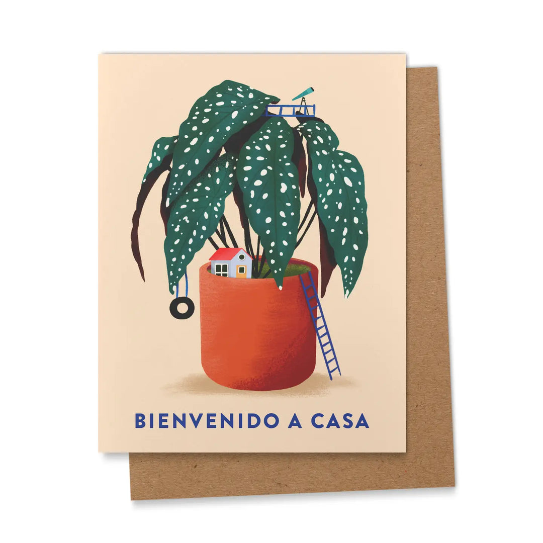 biege card features a home nestled in a begonia plant and the phrase Beinvenido A Casa in blue lettering