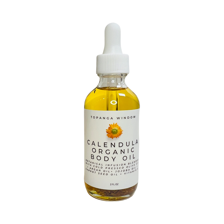 2 oz clear bottle of calendula body oil with a white branded label featuring an image of a single calendula flower. Brand: Topanga Window