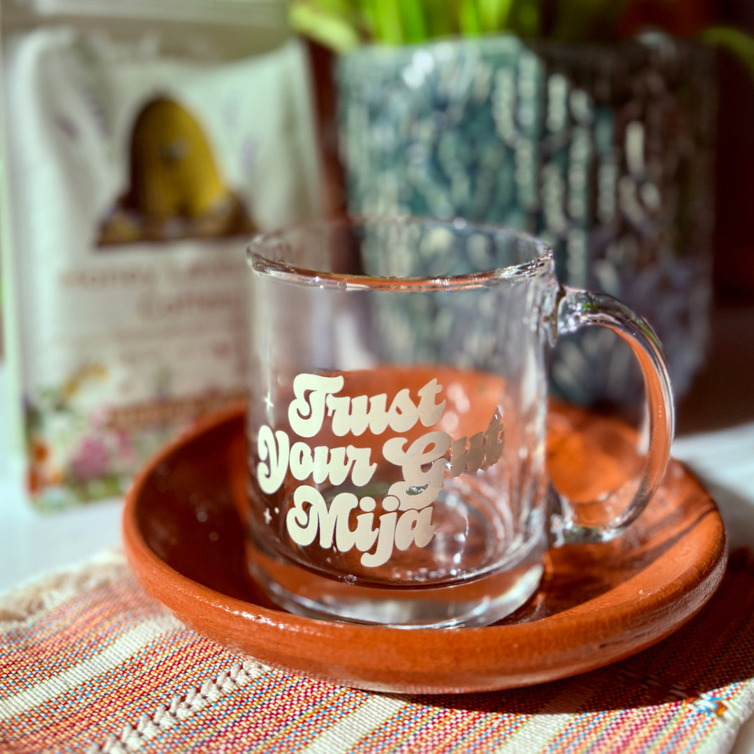 Photo of clear glass mug with the phrase "Trust Your Gut Mija" in ivory, bold, script  lettering with star accents