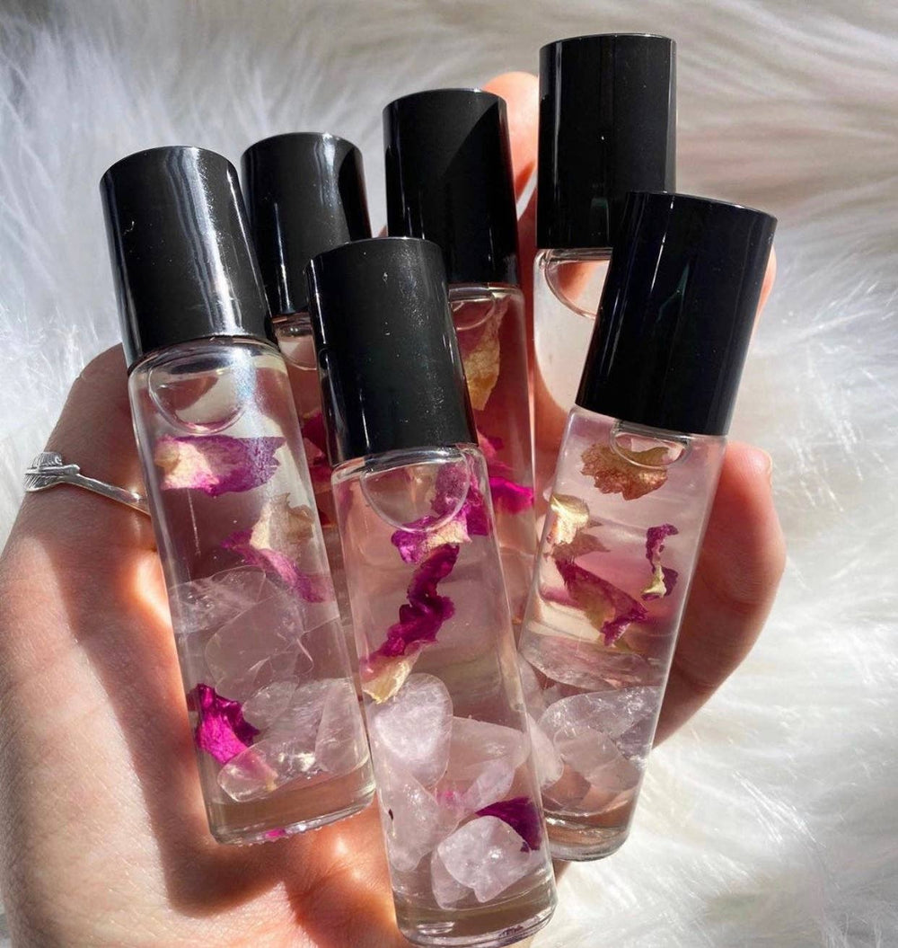 a hand holding 6 clear glass tubes of perfume oil with quartz crystals