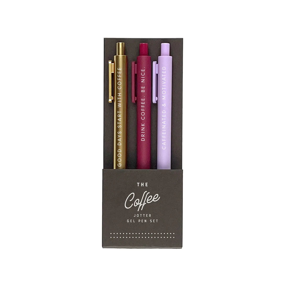 A set of three gel pens in dark brown packaging labeled "The Coffee Jotter Gel Pen Set." The pens come in metallic gold, deep burgundy, and soft lavender, each featuring a coffee-related phrase in white lettering: "Good Days Start with Coffee," "Drink Coffee. Be Nice.," and "Caffeinated & Motivated."