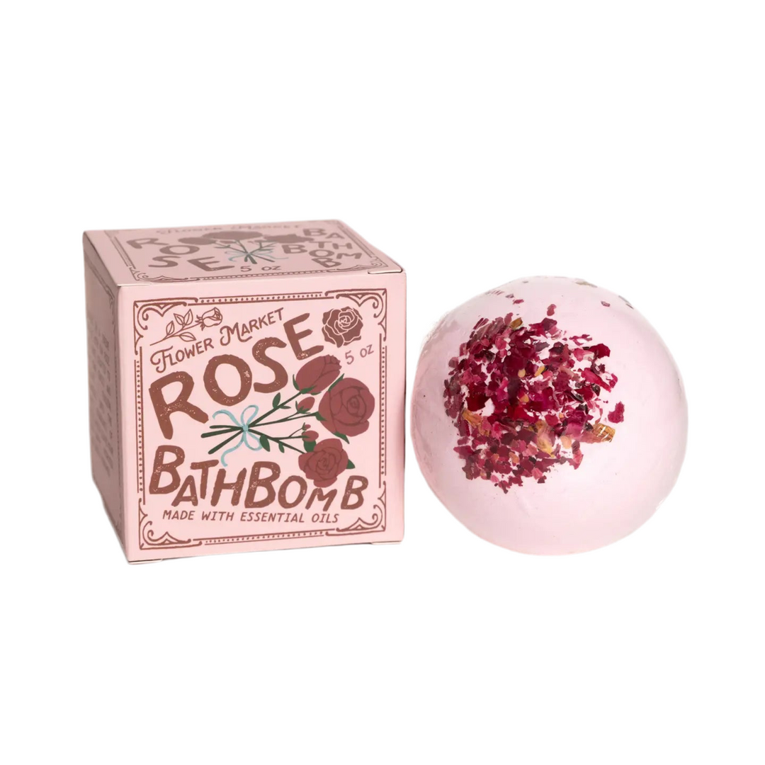 Round pink bath bomb with dried flowers alongside a pink branded box.