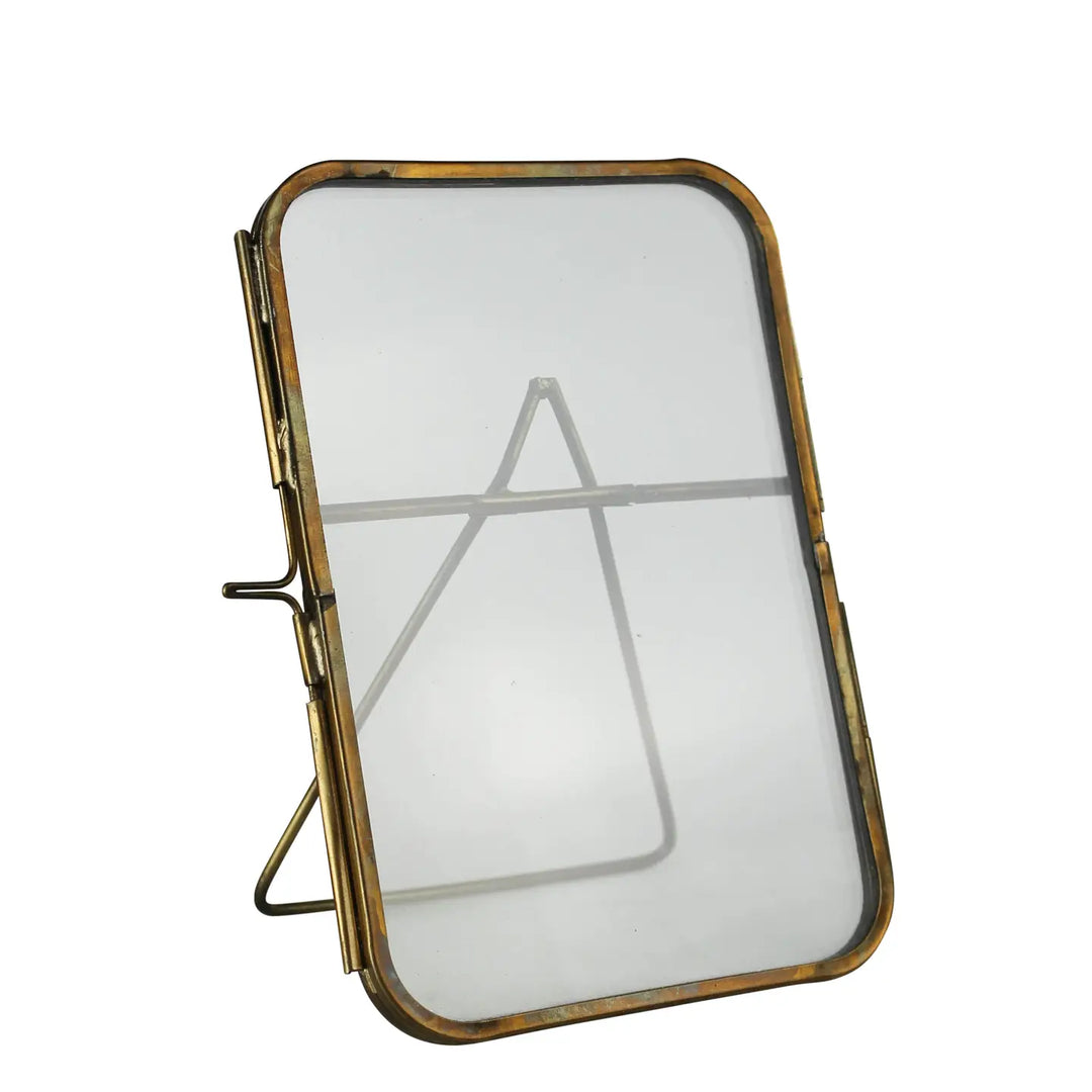 Angled view of a 4x6 picture frame with rounded corners, antiqued brass edges, a glass front, and an easel stand, shown on a white background.