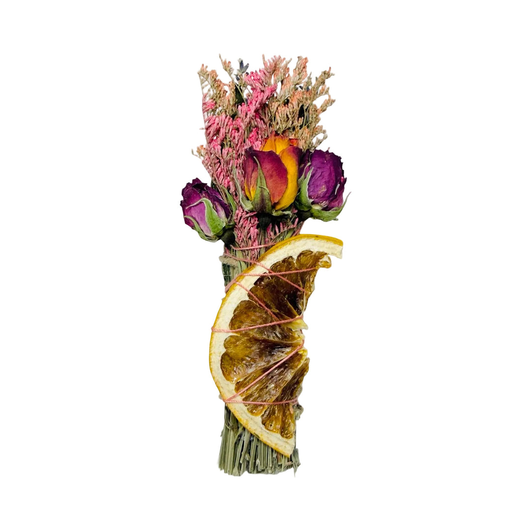 Dried herb smudge stick with roses and a dried grapefruit slice wrapped in pink thread.