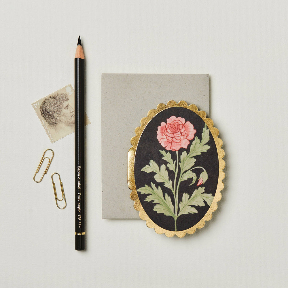 oval black card with a gold scalloped edge featuring a red rose in the center along side a gray envelope, two paper clips, a stamp and a black pencil