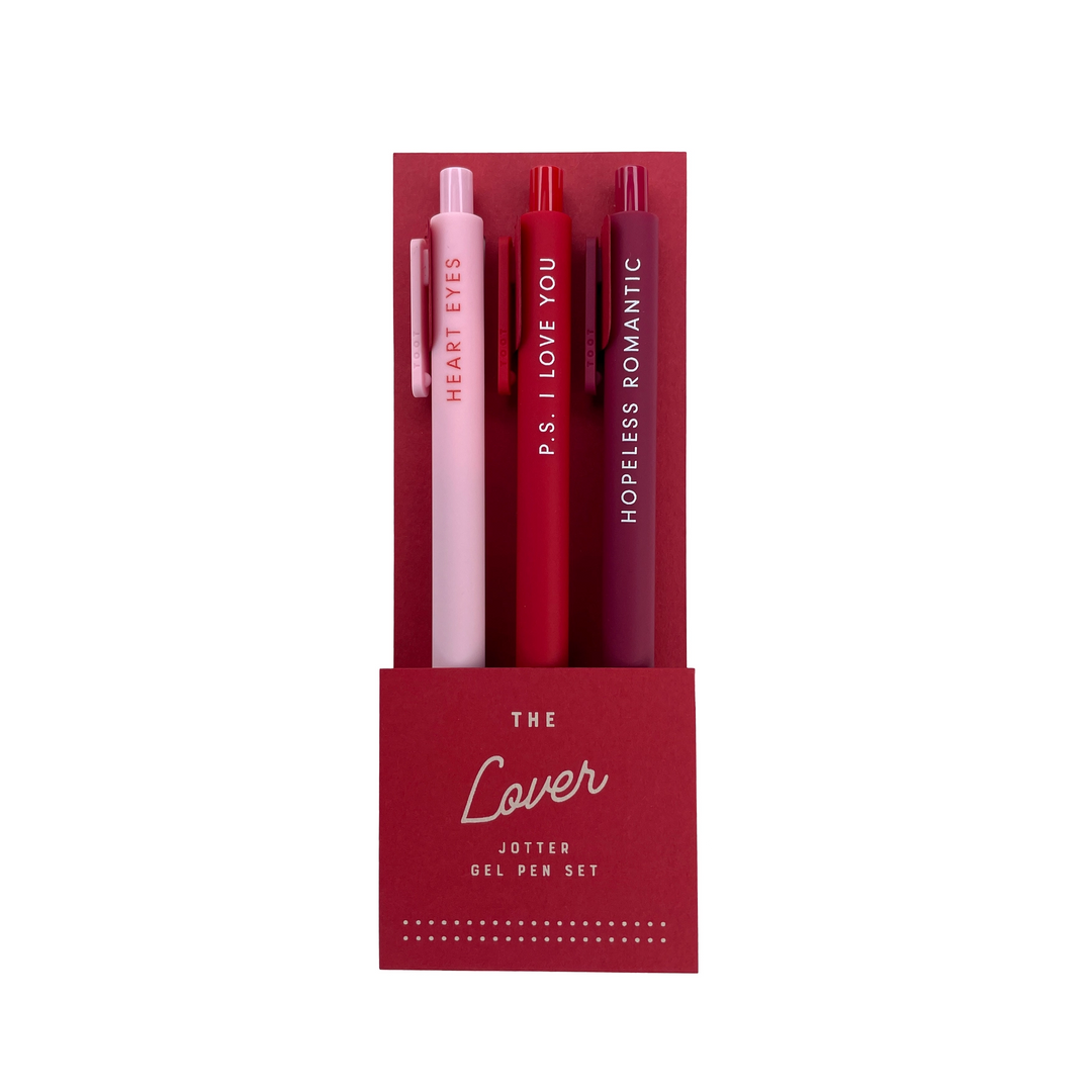 A set of three gel pens in a red packaging labeled "The Lover Jotter Gel Pen Set." The pens come in soft pink, vibrant red, and deep burgundy, each featuring a romantic phrase in white lettering: "Heart Eyes," "P.S. I Love You," and "Hopeless Romantic."