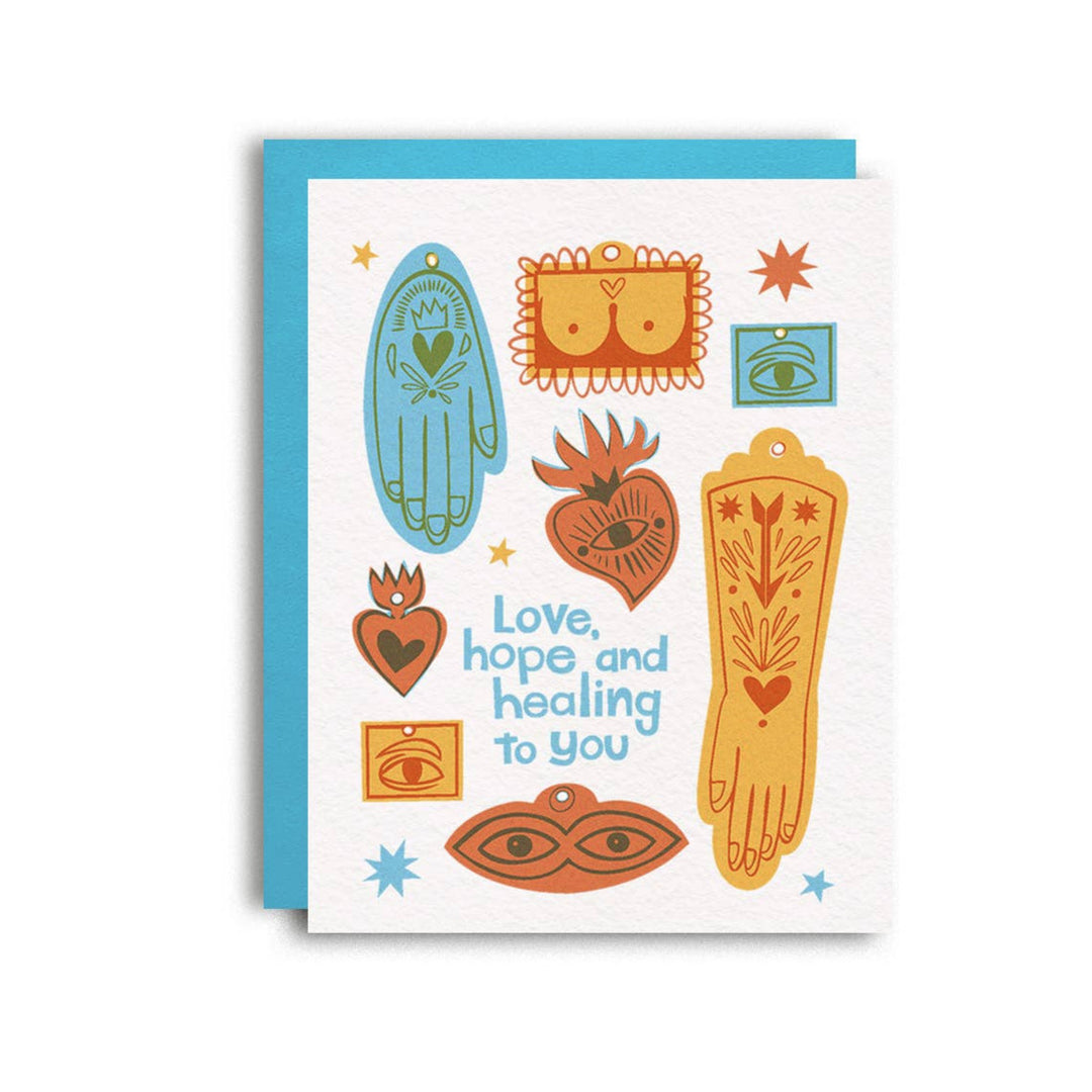 white card and teal envelope with various milagro charms like eyes, hearts, body parts in various colors featuring the phrase Love, Hope and Healing to You in blue lettering