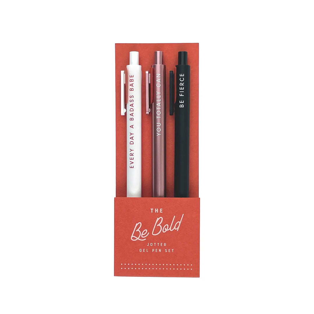 A set of three stylish gel pens in white, rose gold, and black, each featuring bold, motivational phrases, packaged in a chic red box labeled "The Be Bold Jotter Gel Pen Set."