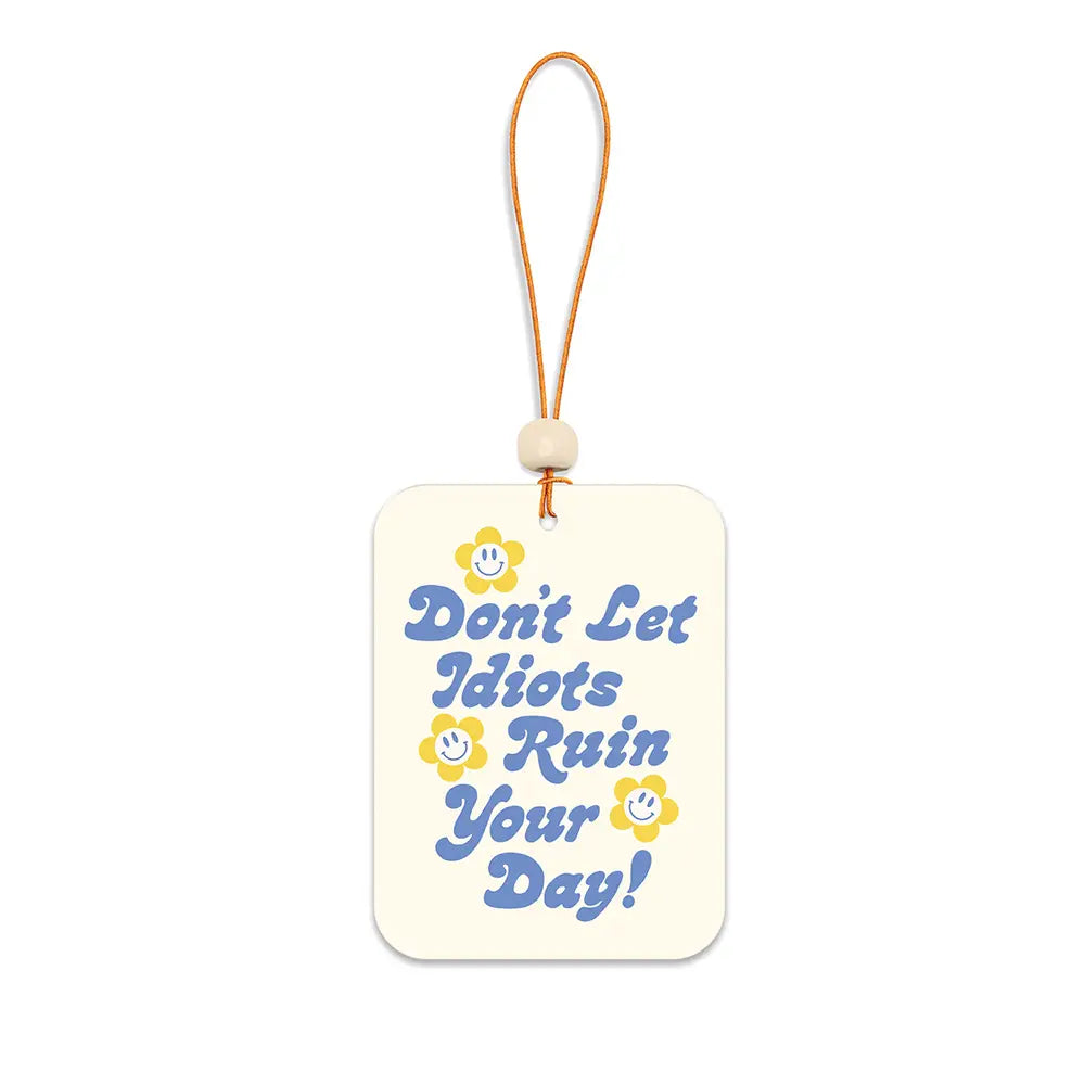 Rectangular car air freshener with a cream background, blue retro-style text that reads “Don’t Let Idiots Ruin Your Day!” and small yellow smiley-face flowers, hanging from an orange string with a wooden bead.