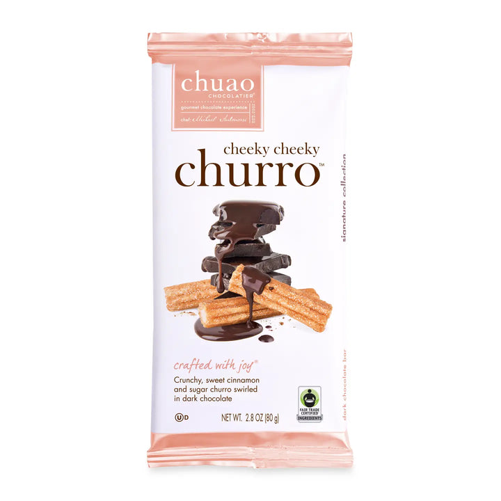 A Chuao Chocolatier Cheeky Cheeky Churro chocolate bar featuring a packaging design with stacked dark chocolate pieces drizzled in chocolate and paired with churros dusted in cinnamon and sugar. The label highlights "crafted with joy" and fair trade certified ingredients.