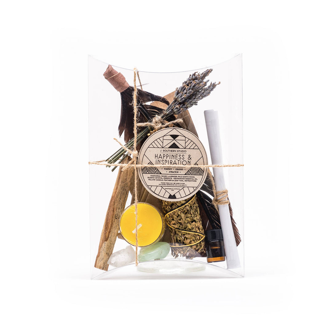 clear box with branded circle brown label and contains dried herbs and flowers, palo santo, lemon oil, candle and turkey feather.