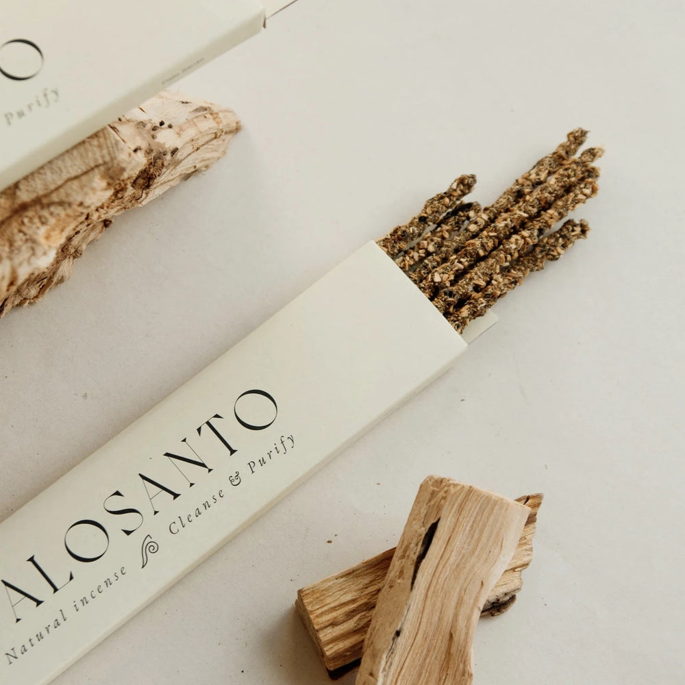 cream colored box of palo santo incense with the sticks of incense sticking out of box. Features two pieces of palo santo.