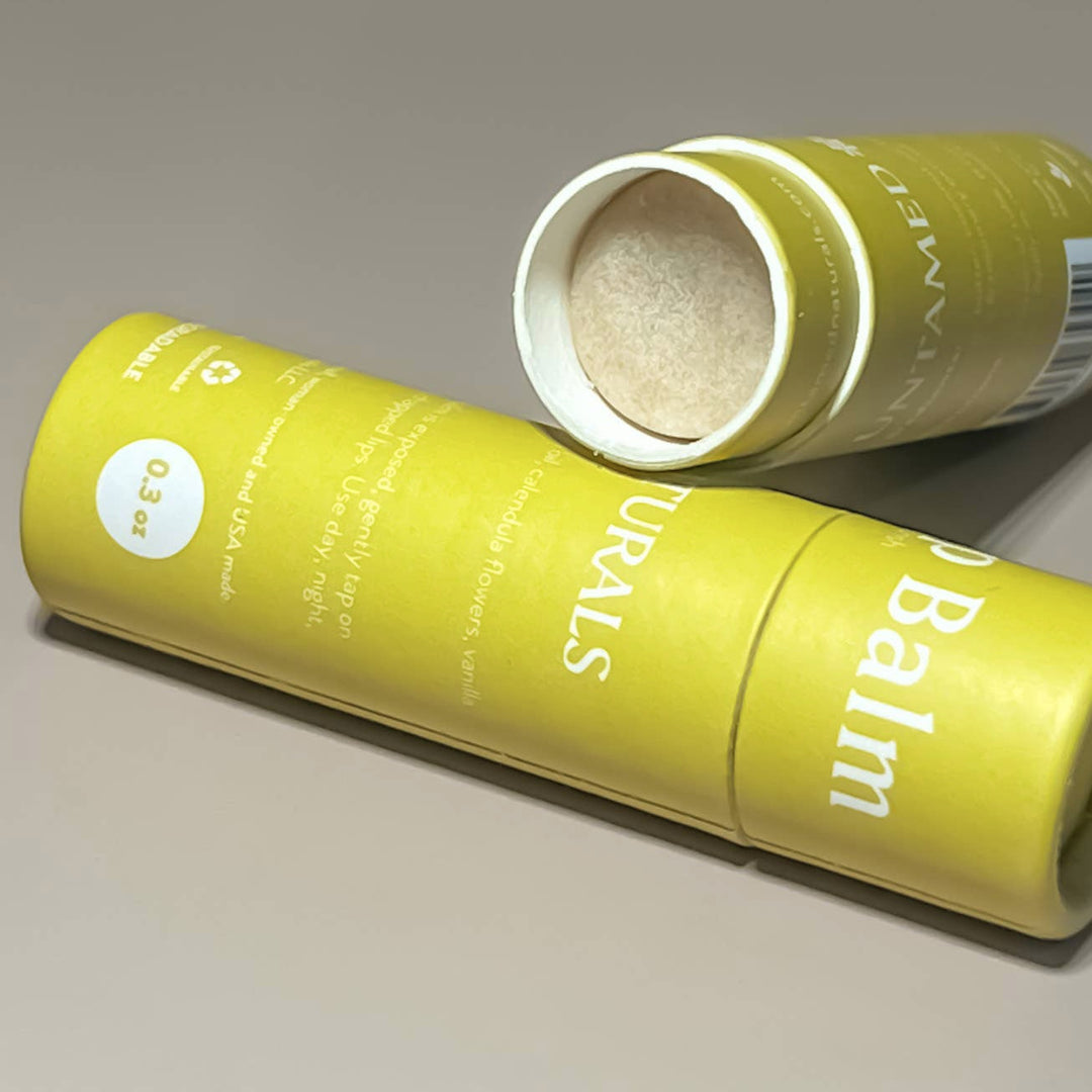 close up view of an open tube of lip balm that is laying on another tube of lip balm that is closed. both have yellow branded labels. Brand: UnTamed Naturals