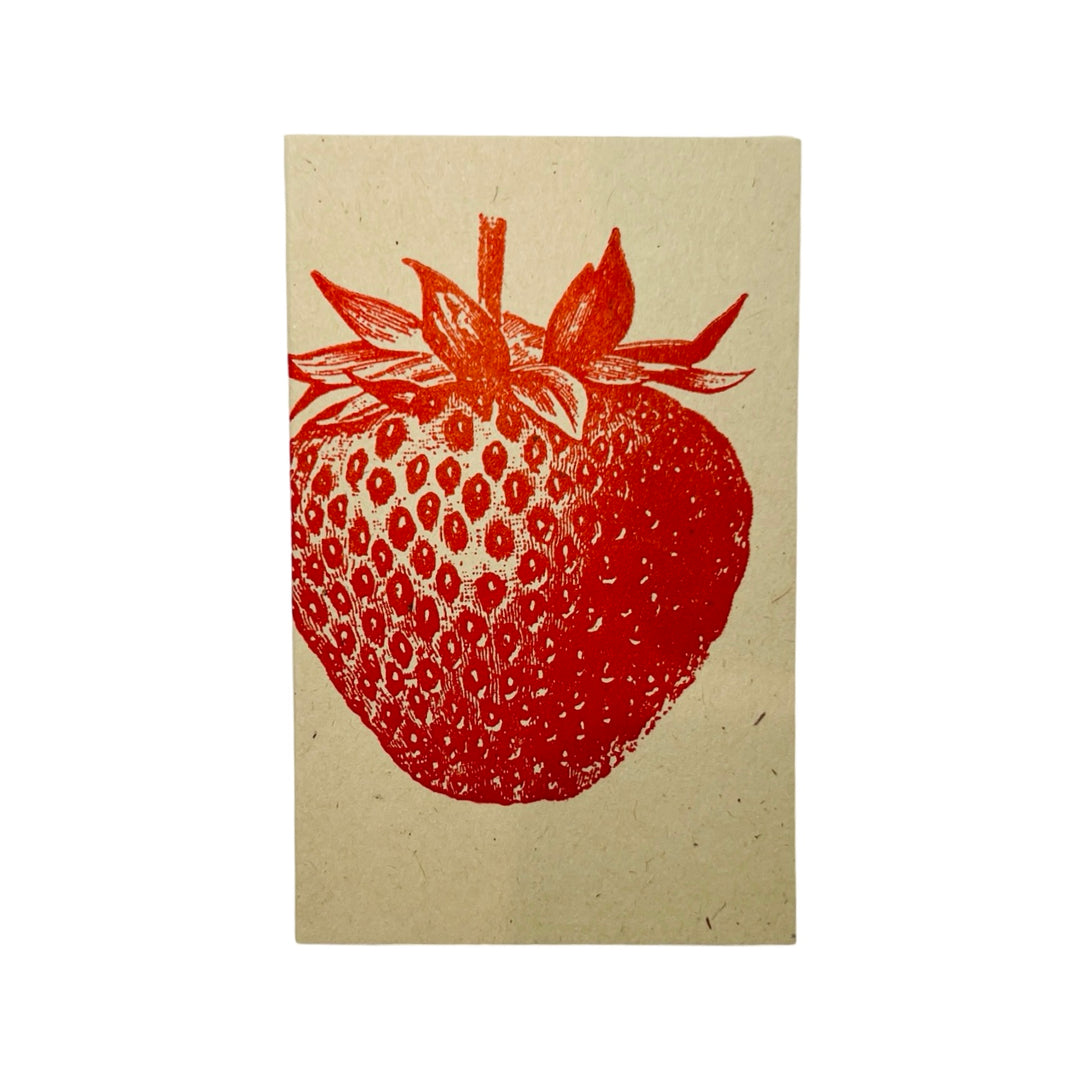 A small folded card with a detailed red strawberry illustration on a textured, natural beige background. The vintage-style print gives it a rustic and organic feel.