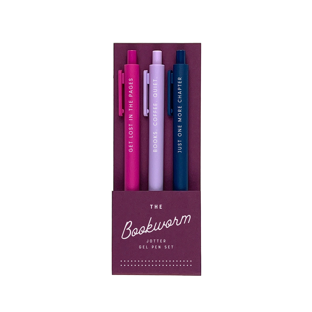 A set of three gel pens in a deep plum-colored packaging labeled "The Bookworm Jotter Gel Pen Set." The pens come in magenta, lavender, and navy blue, each featuring a literary-inspired phrase in white lettering: "Get Lost in the Pages," "Books, Coffee, Quiet," and "Just One More Chapter."