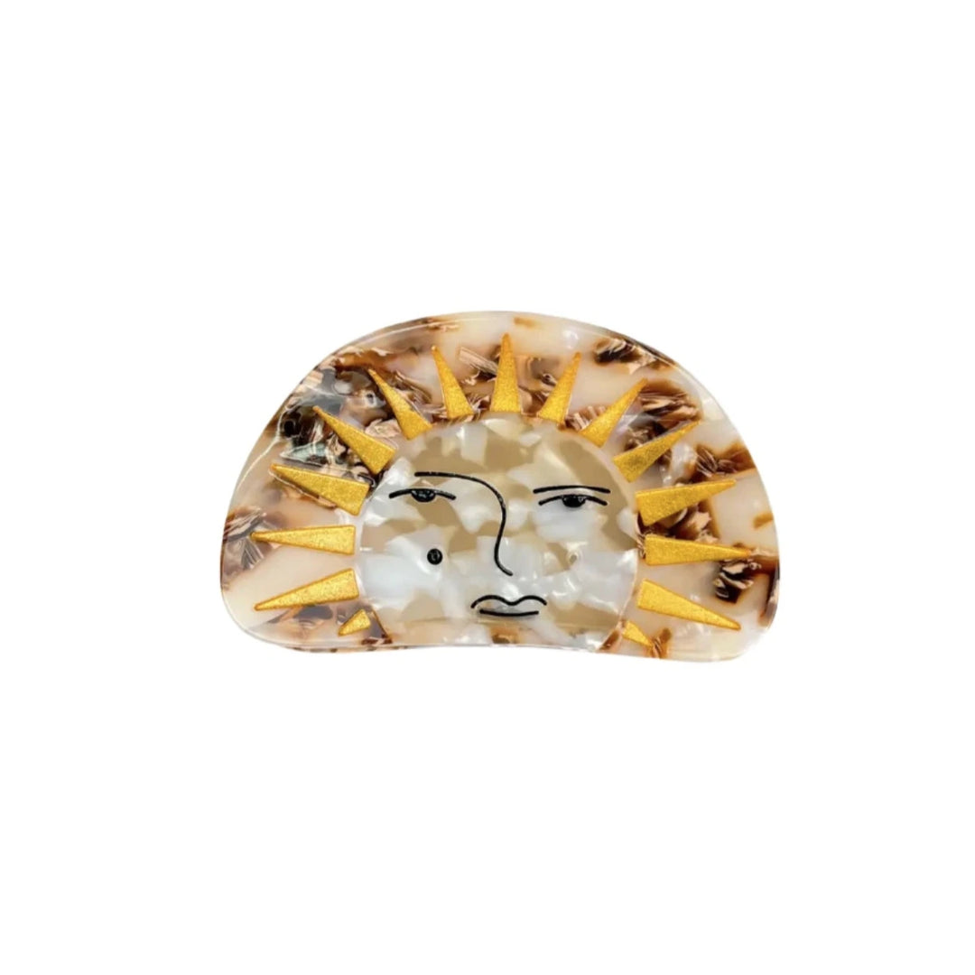 A sun-themed hair clip with a marbled finish, golden sun rays, and an artistic face design, set against a white background.