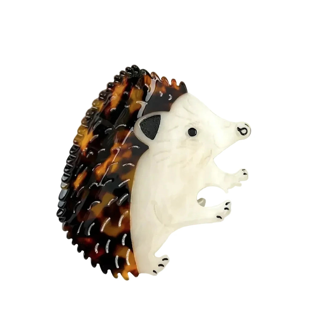 A large acrylic hair claw clip shaped like a hedgehog with a tortoiseshell patterned body and a cream white face and paws.