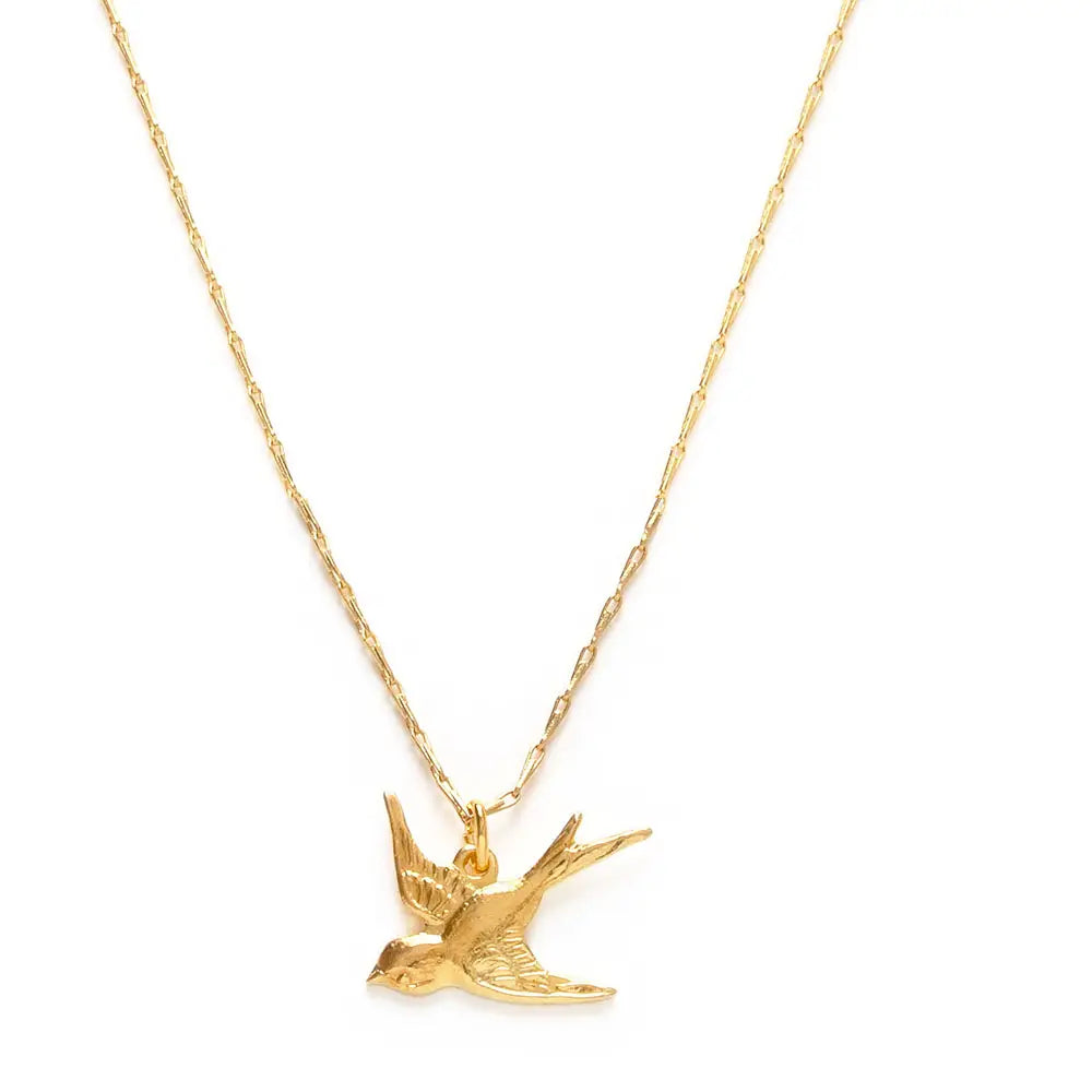 close up view of a gold swallow charm on a gold chain