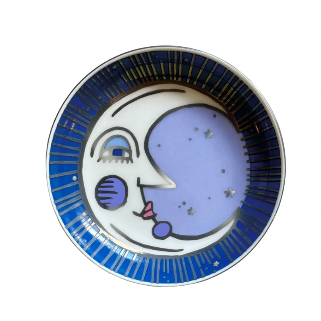 A decorative dish featuring a whimsical moon illustration with a serene face, accented by a deep blue border with gold starburst details.