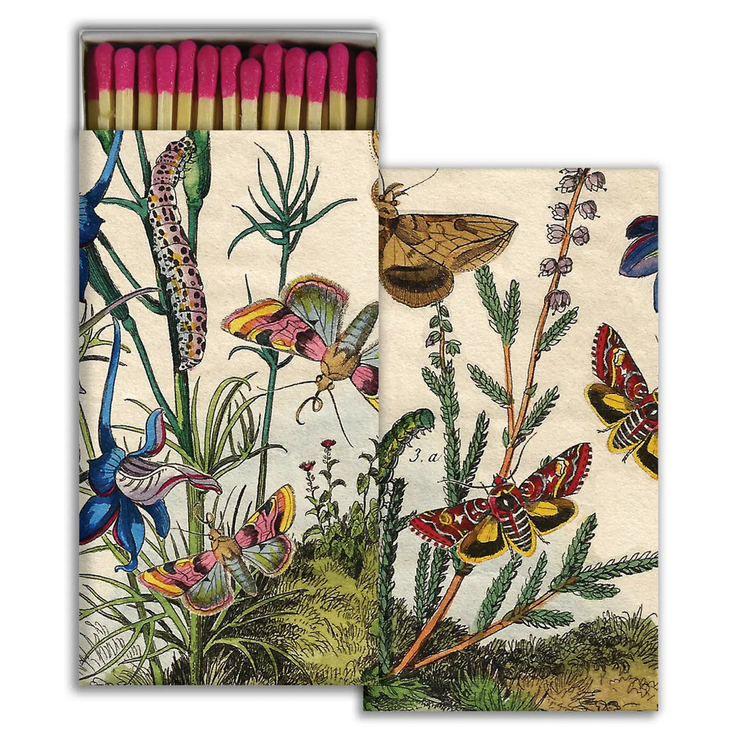 A decorative matchbox featuring a vintage botanical illustration of colorful moths, butterflies, caterpillars, and vibrant plants. The box is open, revealing matches with bright pink-tipped heads neatly arranged inside.