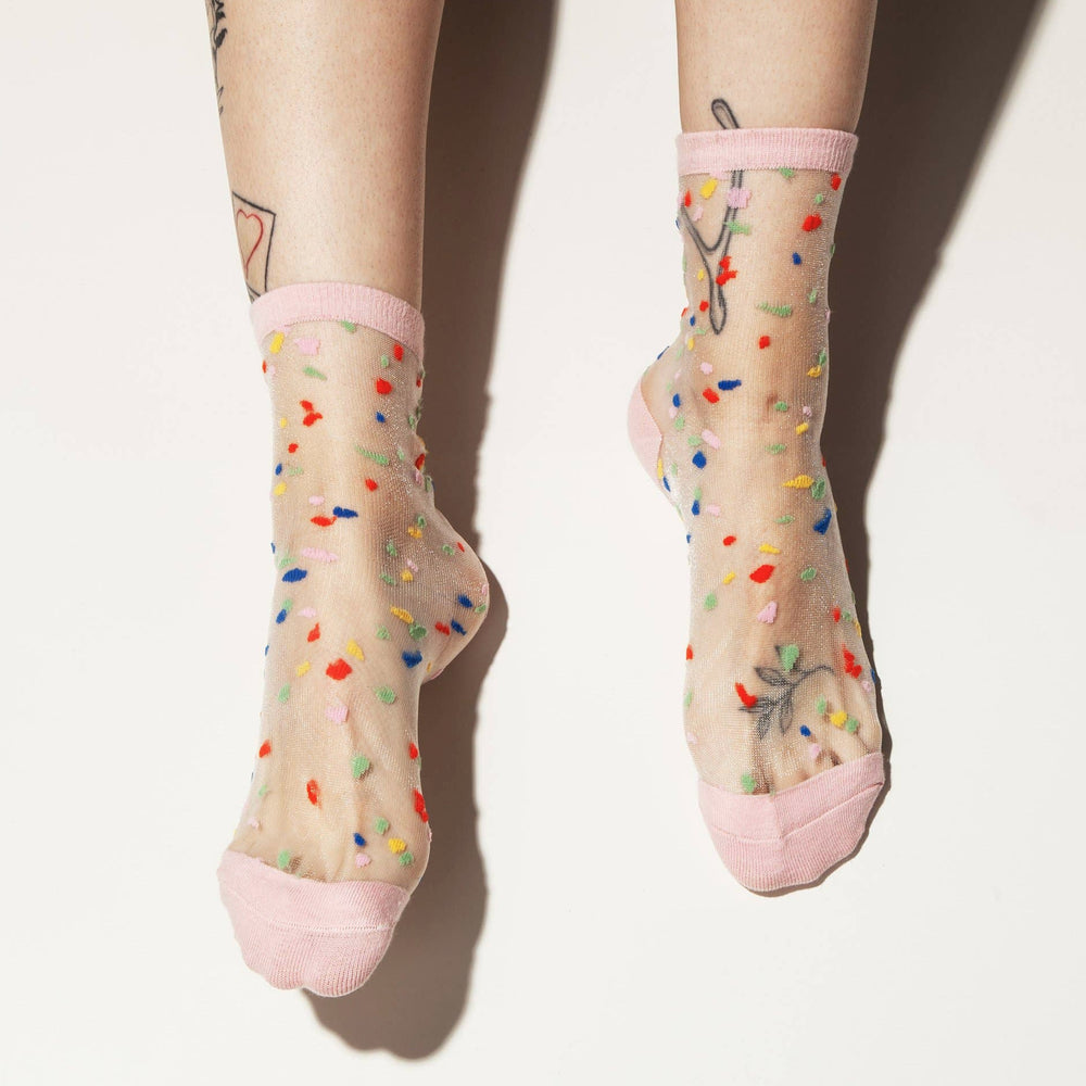 pair of feet wearing A pair of sheer socks with a happy confetti pattern and pink detail