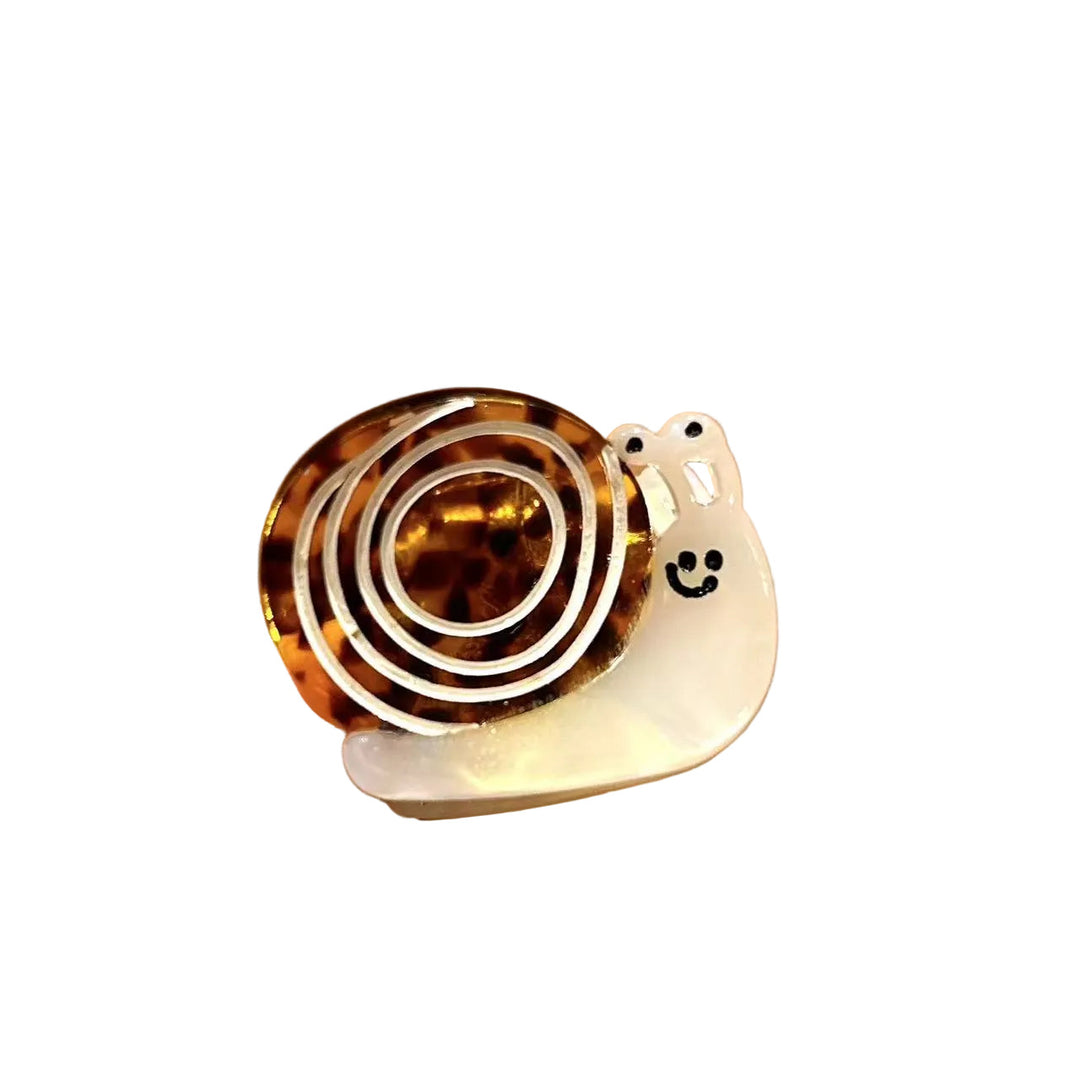A small snail-shaped hair claw clip, featuring a tortoiseshell spiral shell and a white smiley face body.
